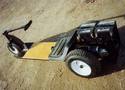 Picture of a low 3-wheeled cart with 2 batteries in the back and a 

t-handle steering arm