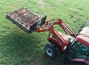 Aerial view of a red tractor in a green field with a bale grabber on the front end loader