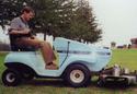 Man riding a light blue electric lawn mower with mower deck attached to front