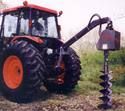 Attached to the tractorâ€™s 3-point-hitch arm (and in the process of digging a post hole) is the device consists of the auger and above it the motor housing.
