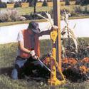 Seen is an adult male on his knees pumping the deviceâ€™s internal hydraulic-pump lever which ratchets up a square wooden post thatâ€™s collared to the device.