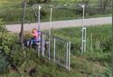 Seen is an adult male on an ATV pulling a rope hanging from the gateâ€™s level arm, which causes the gate to swing back to close position.