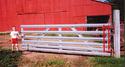 An aluminum, 10-foot-long, six-rail gate with a young male standing at its latching end and a red-metal, 4-foot-tall, angle-adjusting hinge secured to the gate that affixes it to the gate post at the other end.