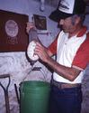 Holding up with his right hand the spring scale with feed bucket attached, an adult male feels the scaleâ€™s raised marks with the finger of his left hand to determine the weight.