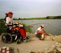 An adult male in his wheelchair, the motorized rod hinged and reel bolted to a board extending out from the chair and the vacuum tubes running from rod/reel to his mouth area.