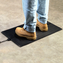 A person's legs from the calf down wearing blue jeans and work boots standing on a Foot Warmer Mat on a hard-surface floor