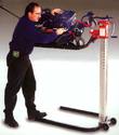 An adult male working on a mower secured to the lift platform that has been raised to shoulder height and tilted somewhat for easier reach.