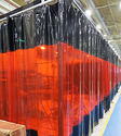 Large plastic curtain hanging in welding shop. Curtain is black on top and bottom and see-through red in middle.