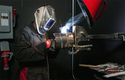 Man welding with helmet, exhaust fan, gloves, and protective work clothes