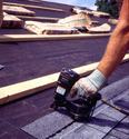 An adult male is using the tool as described to shingle a roof.