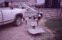 The operator is seen in the tractor cab, having already transferred from his wheelchair on the platform at the end of the lift, which extends from pickup bed to tractor-cab door.