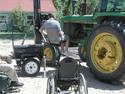 Having already transferred from his wheelchair to the two-wheel trailer-mounted left chair, an adult male is being elevated to his tractorâ€™s cab.