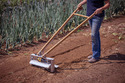 Person from chest down wearing bluejeans and guiding the seedbed tilther along a garden row