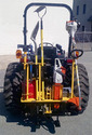 picture of the back end of a tractor in a parking lot with a yellow metal rack mounted on the back holding numerous garden tools like a rake, shovel, weed-whacker, chainsaw, gas can, and axe