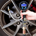 Side of tire rim with disk brake behind rim and a hand holding a digital tire gauge-inflator hooked to the tire inflation valve via a short hose