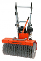 Black gasoline engine mounted on silver tubular frame of 2 push-handles with bright orange cover over rotary broom mounted on the front. Broom bristles are on a horizontal shaft.
