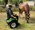 Person sitting on OMEO wheelchair next to a horse in a wire-fence enclosure