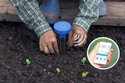 2 hands putting a blue-capped instrument with 2 prongs into a dirt bed & there is a round picture insert of a hand holding a phone with data on it