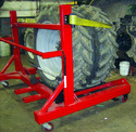 Large dual tractor tires sitting on a red heavy horizontal metal frame with a castor wheel on each of 4 corners. 2 uprights on one end of frame have yellow arms at top that keep tires from rolling off frame