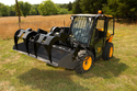 Yellow & black skid loader in field with black add-on grapple with 4 grapples o
ver top of loader bucket.