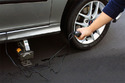 Right front tire on silver car with black electric cord coming from car door to silver jack under frame of car and an arm holding the control for the electric jack
