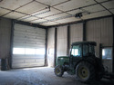 John Deere tractor sitting inside shed facing closed overhead door with powered door opener fastened to shed ceiling above tractor