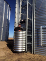 Man standing inside a corrugated metal elevator that is open from his chest up to ride up the side of a round metal grain bin.