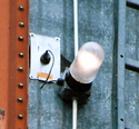 A light mounted on the side of a metal grain bin with a wire going to a sensor on the inside of the grain bin
