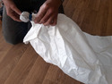 Person kneeling on wood floor holding large white plastic bag with stone tied in end of it and held with rubber band