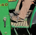 Person's left leg below knee pushing on stirrup attached to clutch pedal on John Deere tractor.