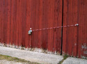 Red sliding barn door with hand-crank cable winch mounted to it and the cable stretching to side of barn where it is attached to an eye hook.
