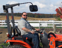 Man on orange Kubota tractor with a ROPS-mounted mirror on the right side.