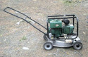 A silver push mower with a green generator mounted on the body where the mower engine would normally be.