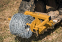 Yellow fence wire unroller with a roll of barbed wire on it attached to back of garden tractor