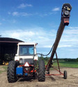 White tractor in front of large shed with auger mounted to tractor & hydraulic hoses attached.