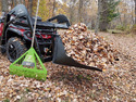 Red & black ATV with lawn debris basket mounted to it & green leaf rake leaning against it