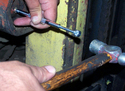 A right hand hammering a grease-fitting cleaning tool held in the left hand against a grease fitting