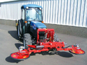 Blue tractor with red double-sided orchard mowing attachment mounted on the front of it.
