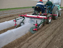 Low-Tunnel Layer Machine pulled behind a tractor laying down plastic low-tunnels on a prepared dirt bed