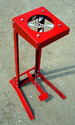 A Produce-Bunching Rubber Band Applicator painted red and sitting on sand and gravel