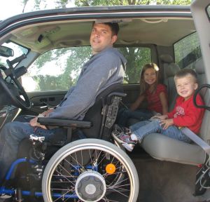 Eric Beckman sitting in wheelchair in pickup truck with his kids in back seat