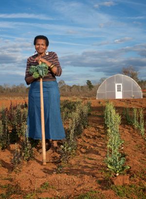 Ruby Davis stands with a hoe in a field in front of a greenhouse