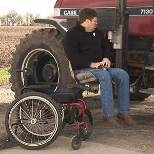 R.D. Elder riding lift up to cab of tractor with wheelchair in foreground