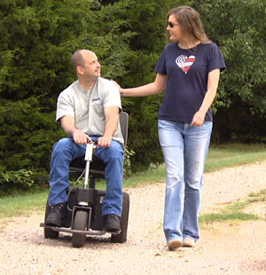 John Enns on scooter with wife Charla walking next to him.