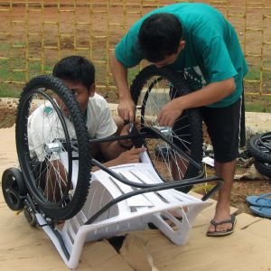 Two young men in India constructing wheelchair out of plastic lawn chair and bicycle tires