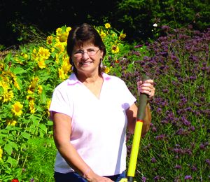 Terrie Webb holding rake in front of red and yellow flower crops