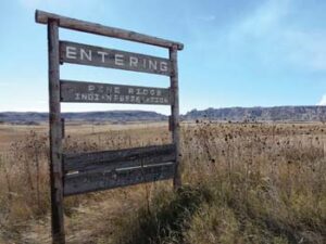 Wooden sign in foreground that says, "Entering Pine Ridge Indian Reservation." Mountain range in background.