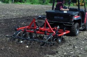 Cultivator on back of utility vehicle being used to break up ground.