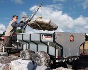 Man using Boom Lift on trailer to hoist large rock into trailer.