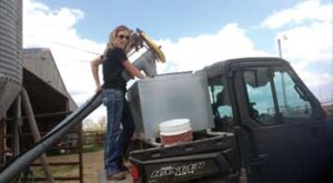 Carey standing on rear of utility vehicle using an auger to put feed into feeder located on back of UTV